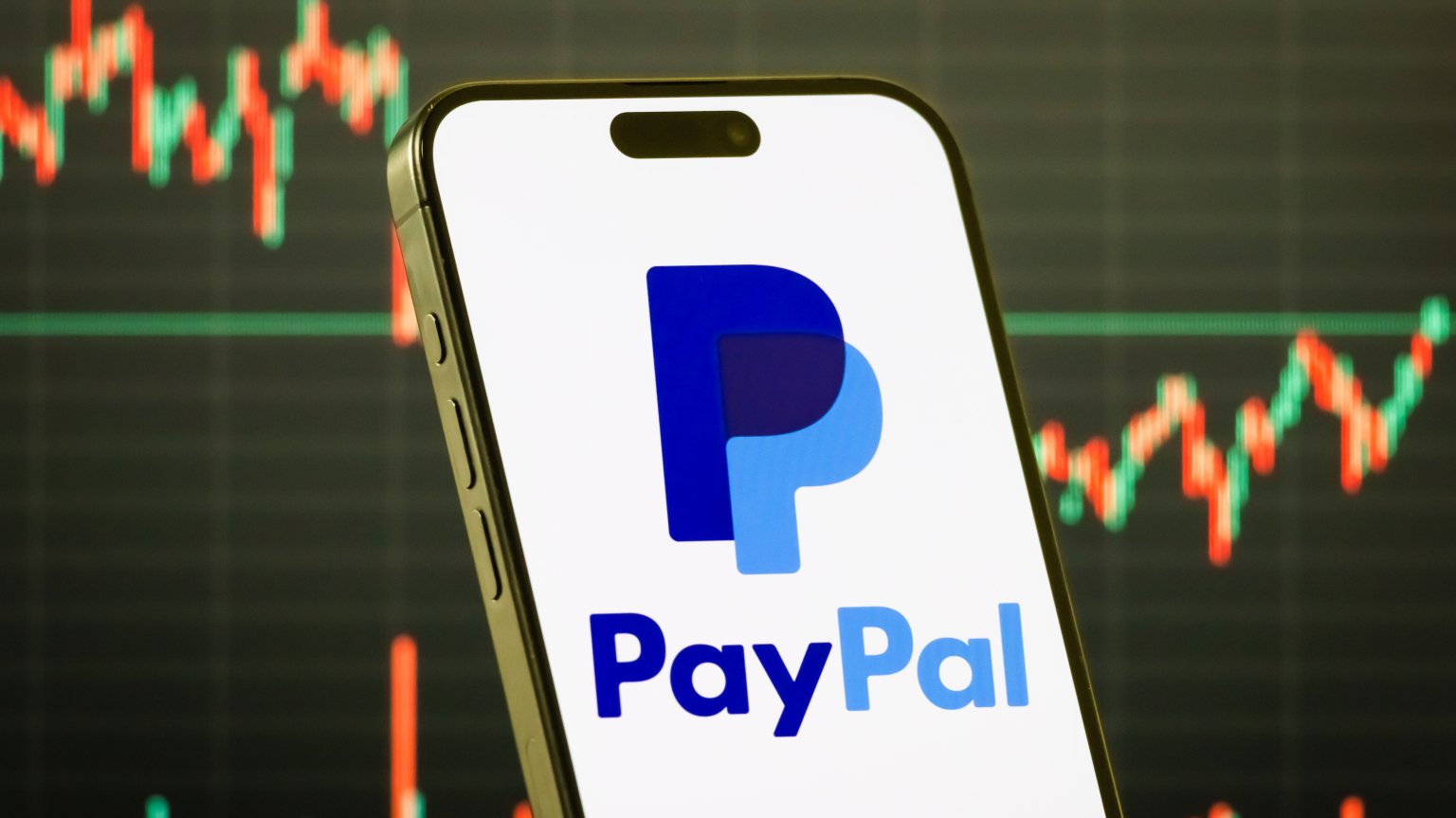 a smartphone displays the PayPal logo in front of a screen showing stock market gains