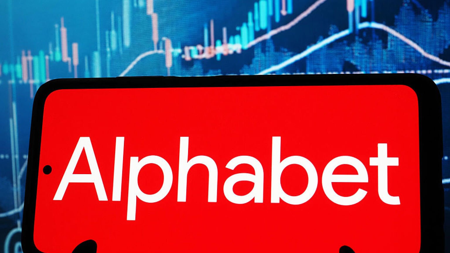 Alphabet logo on smartphone screen in front of stock charts