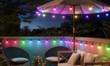 the govee smart outdoor string lights 2 on a back patio, displayed around the bottom permitter of a sun umbrella over a table and along a deck railing