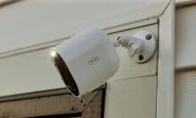 an arlo spotlight camera sits on the outside of a home, near the garage and is covered in rain drops
