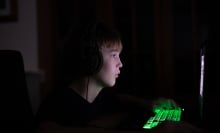 A tween or teen boy looks at a computer screen in a darkened room. 