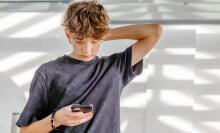 A teen boy looks down at his phone. 
