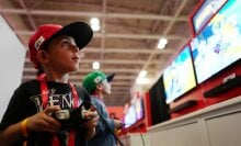 Two small children wearing Nintendo merch play a new Switch 2 game in front of large monitors. 