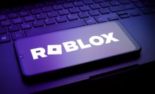 A phone displaying the Roblox logo in dark moody lighting.