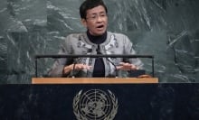 At the UN podium, a woman with short hair and glasses speaks. 