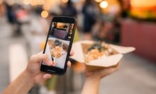 A woman takes a photo of her food at a market using a smartphone.