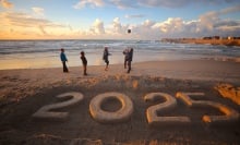Children on a beach playing with a ball by a '2025' sand sculpture