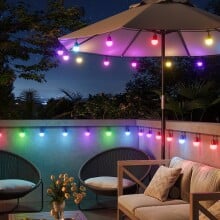 the govee smart outdoor string lights 2 on a back patio, displayed around the bottom permitter of a sun umbrella over a table and along a deck railing