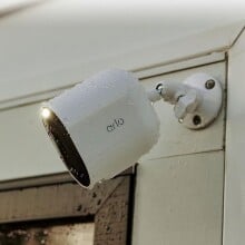 an arlo spotlight camera sits on the outside of a home, near the garage and is covered in rain drops