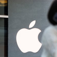 A woman, blurred in the foreground, walks by an Apple store.