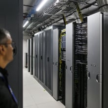 A man stands looking at a bank of AI data processors.