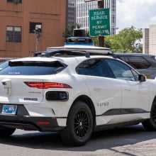 A Waymo midsize SUv parks in a lot in front of a "permit only" sign.