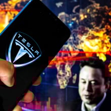 Tesla logo on mobile device with Elon Musk in the background