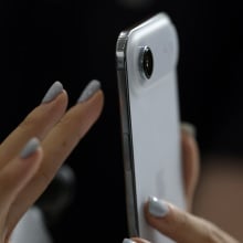 A hand with painted nails taps on the screen of a new iPhone Air.