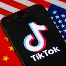 a tiktok logo on a phone with the american and chinese flags behind it