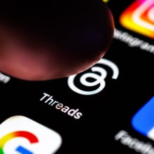 a finger pressing the threads icon on a phone