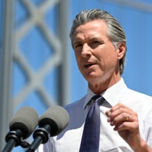 California governor Gavin Newsom speaks at a podium in front of the Bay Bridge.