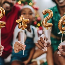 Festive family celebrating the new year at home, holding golden balloons with the numbers 2026. Christmas tree and holiday decorations in the background, joyful and warm atmosphere. Concept of family togetherness, holidays, festive season, new beginnings, 2026 celebration