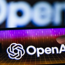 A thumb taps on a phone screen displaying a colorful OpenAI logo.
