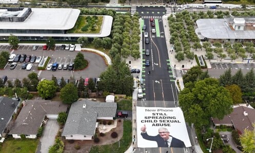 An overhead shot of large white banner unfurled on a street, with an image of Tim Cook and the text "New iPhone still spreading child sexual abuse."