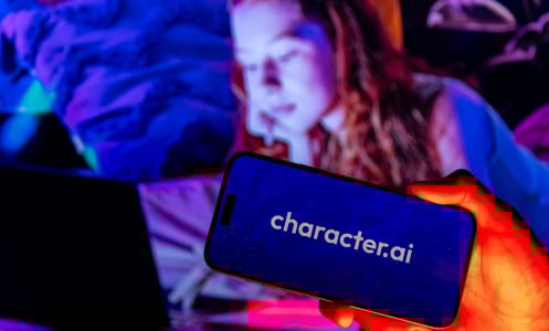 A child looks at a computer with a phone in the foreground bearing the Character.AI logo.