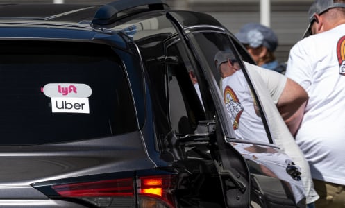 A person gets into the back of a dark car with stickers advertising Uber and Lyft. 