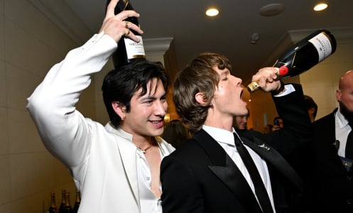 Connor Storrie and Hudson Williams, stars of Heated Rivalry, pose with bottles of champagne. 