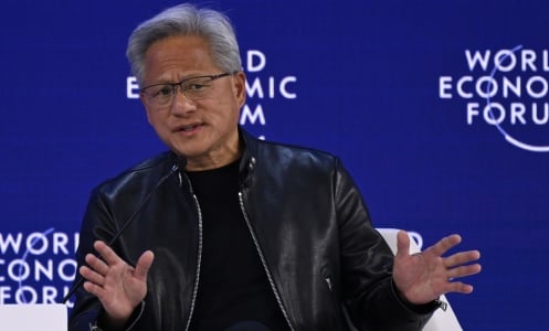 NVIDIA's Jensen Huang making a two handed wave gesture while talking on a World Economic Forum stage