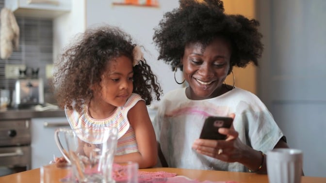 Parent and child sit at a table looking at a phone