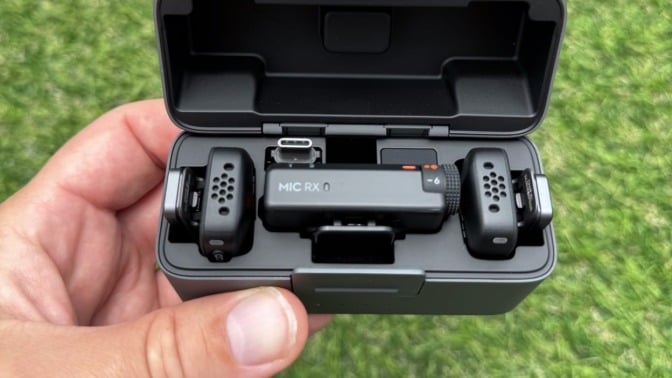 the DJI Mic Mini bundle in a person's left hand with green grass in the background