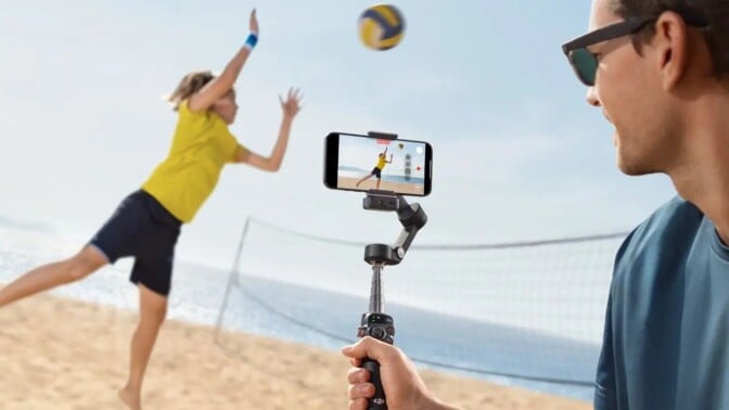 a person holds the DJI Osmo Mobile 7p gimbal while filming a person playing beach volleyball.