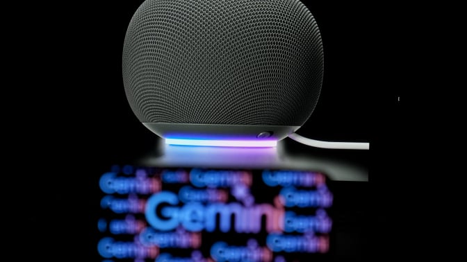  the Gemini logo is displayed on a mobile phone screen in front of a Google smart speaker