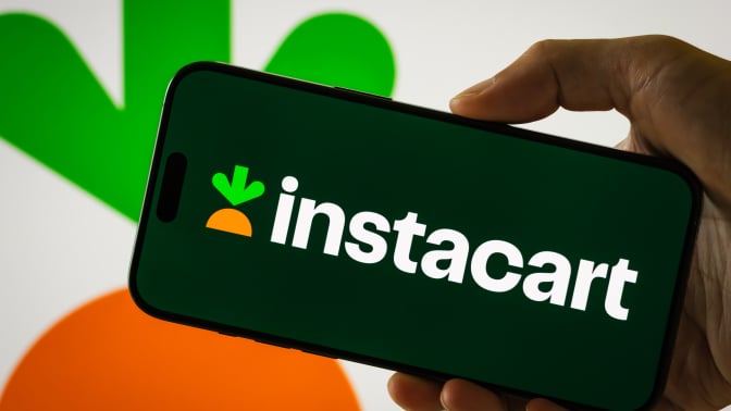 person holds a smartphone displaying Instacart logo
