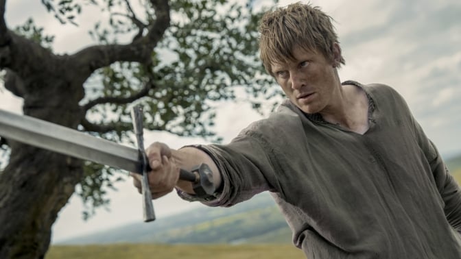 A man stands next to a tree, pointing a sword.