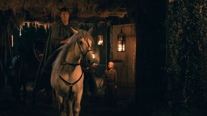 A man sits on a horse outside an inn at night, while a young boy looks up at him.
