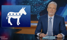 A man in a suit sits behind a talk show desk looking angry. In the top left is the logo of the Democrat party.