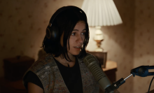 A woman sits in a room wearing headphones.
