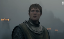 A man in armour sits on top of a horse on a battle field.