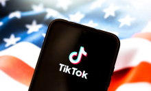 The TikTok logo appears on a smartphone screen, with the American flag on a computer screen in the background.