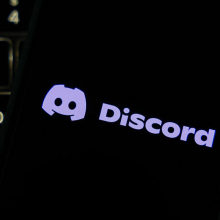 The Discord logo on a smart phone, resting on a computer keyboard.