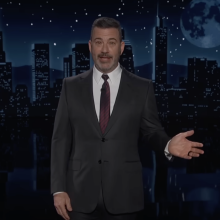 A man in a suit stands on a talk show stage.