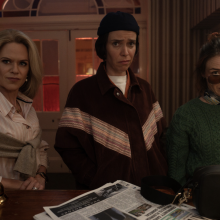 Three women stand in front of a hotel reception counter.