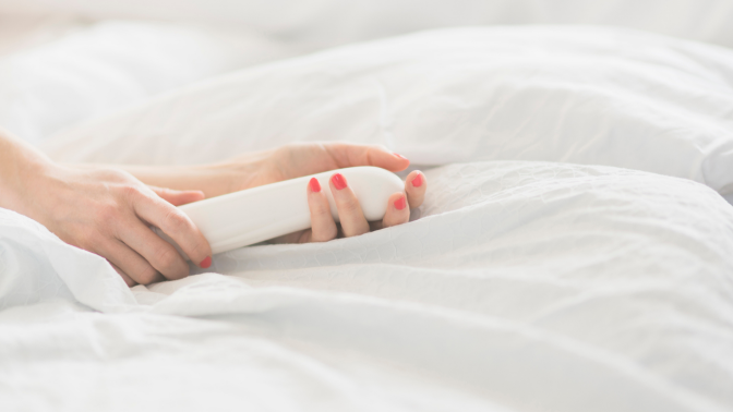 Hand of woman holding sex toy in bed